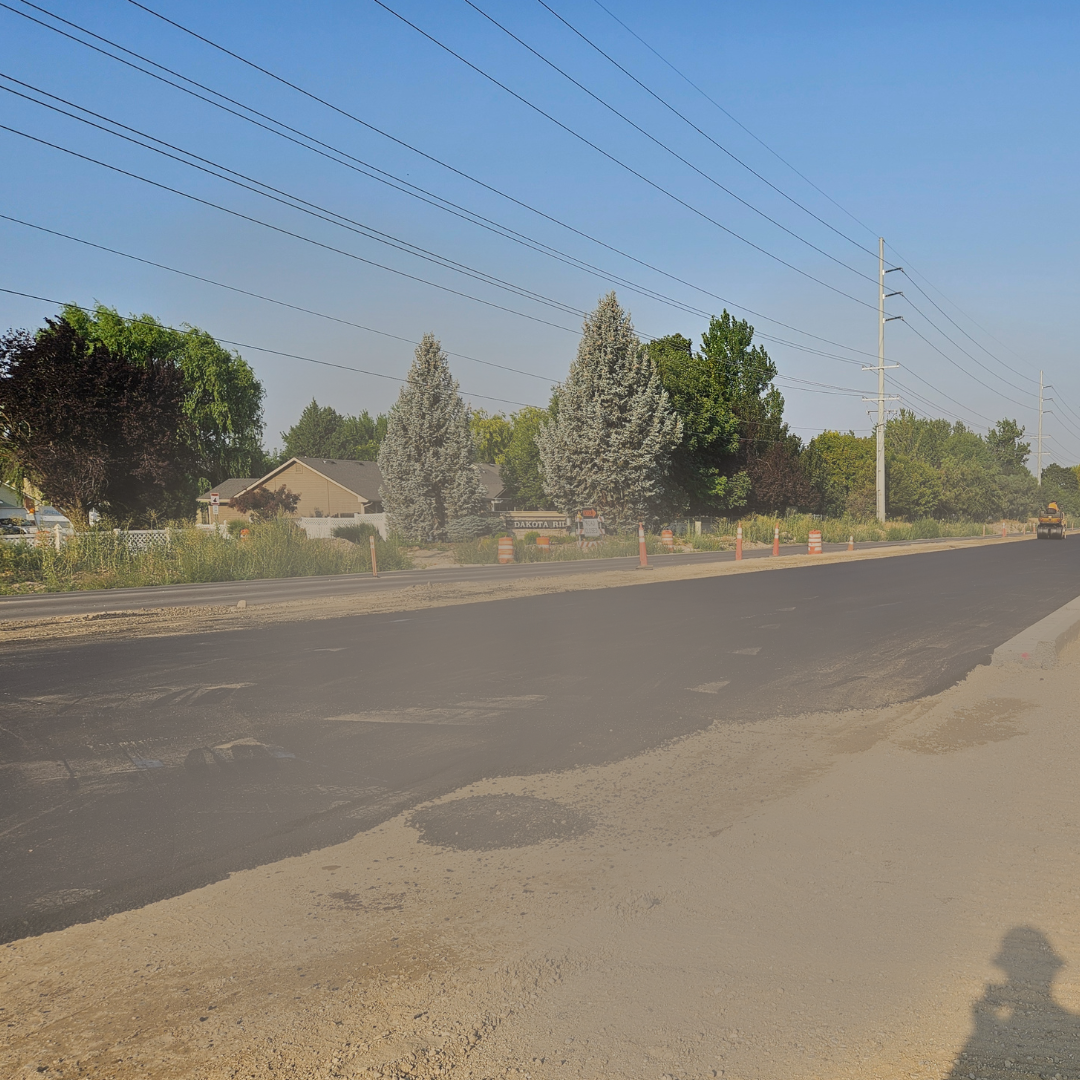 Pavement being smoothed by a roller truck with dust in the air
